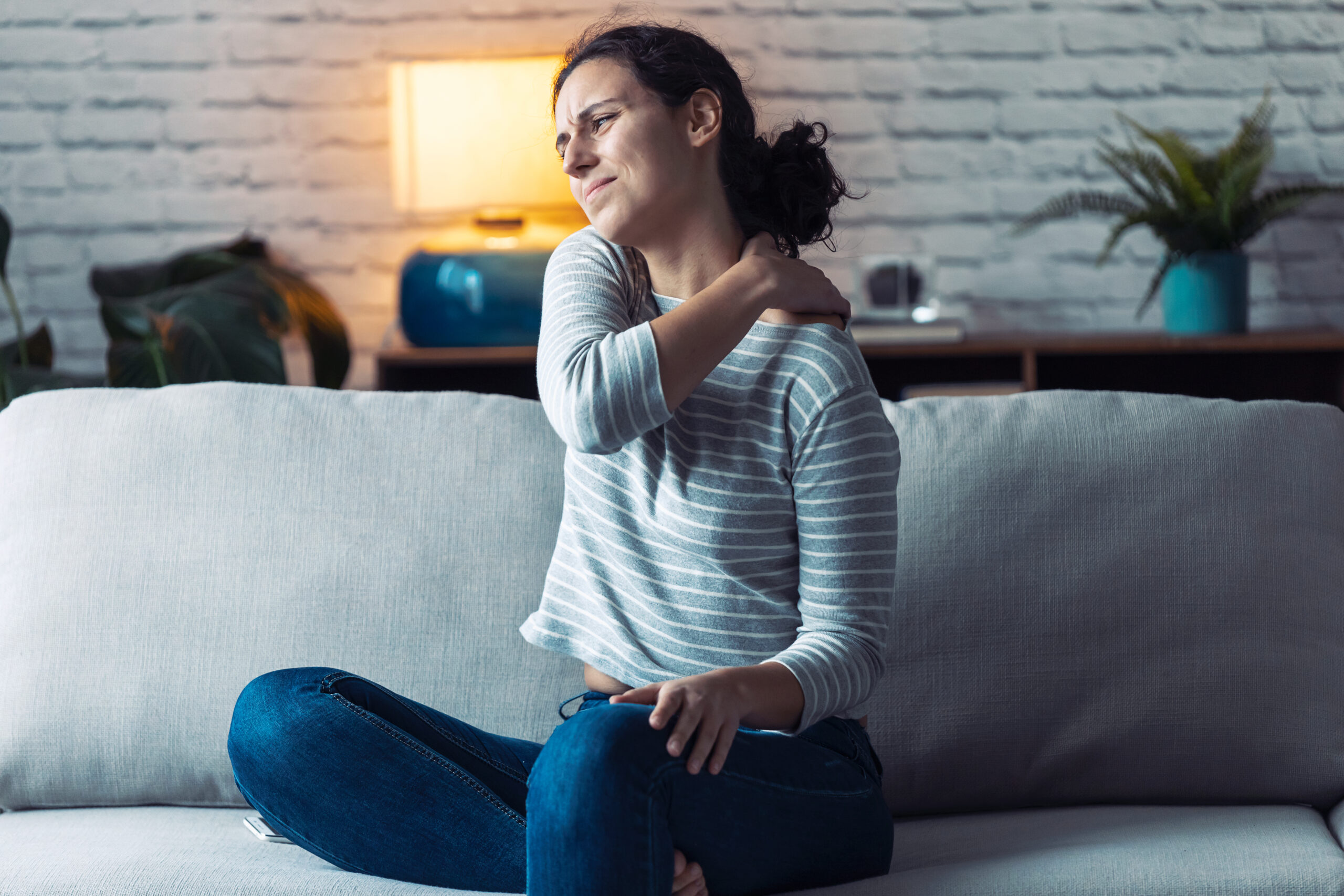 Portrait of a young woman with back Pain sits down on Sofa at Home